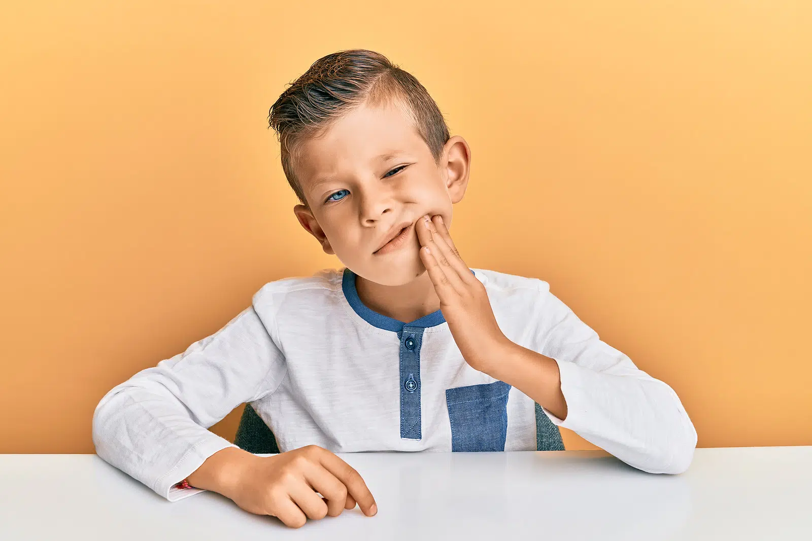 A young boy holding his mouth in pain and in needd of emergency dentistry in Queens, NY