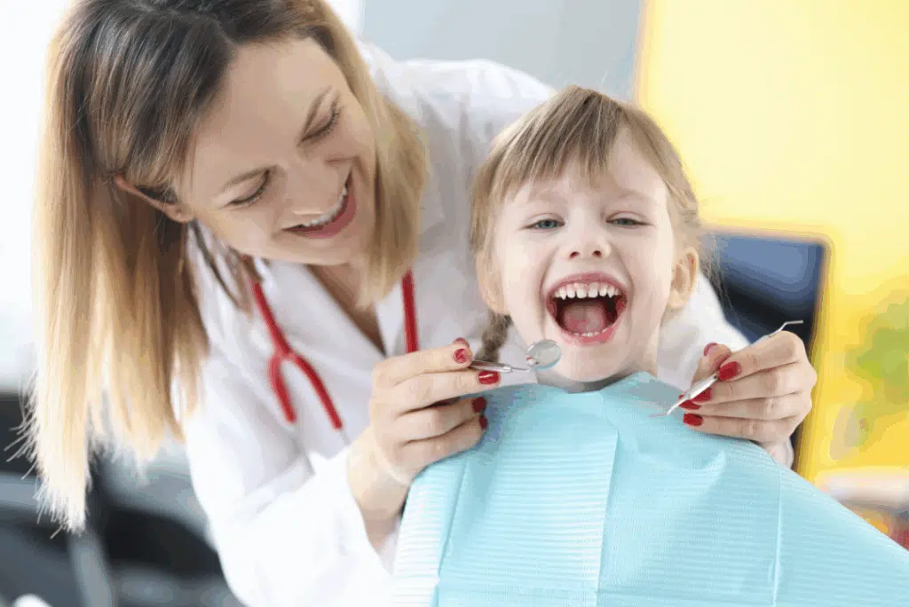 Pediatric Dentist In Great Neck, Ny: A Parent’s Guide To Expert Dental Care For Kids Child smiling in dental chair with pediatric dentist holding dental tools, showcasing a positive dental experience at PCO Pediatric Dentistry.