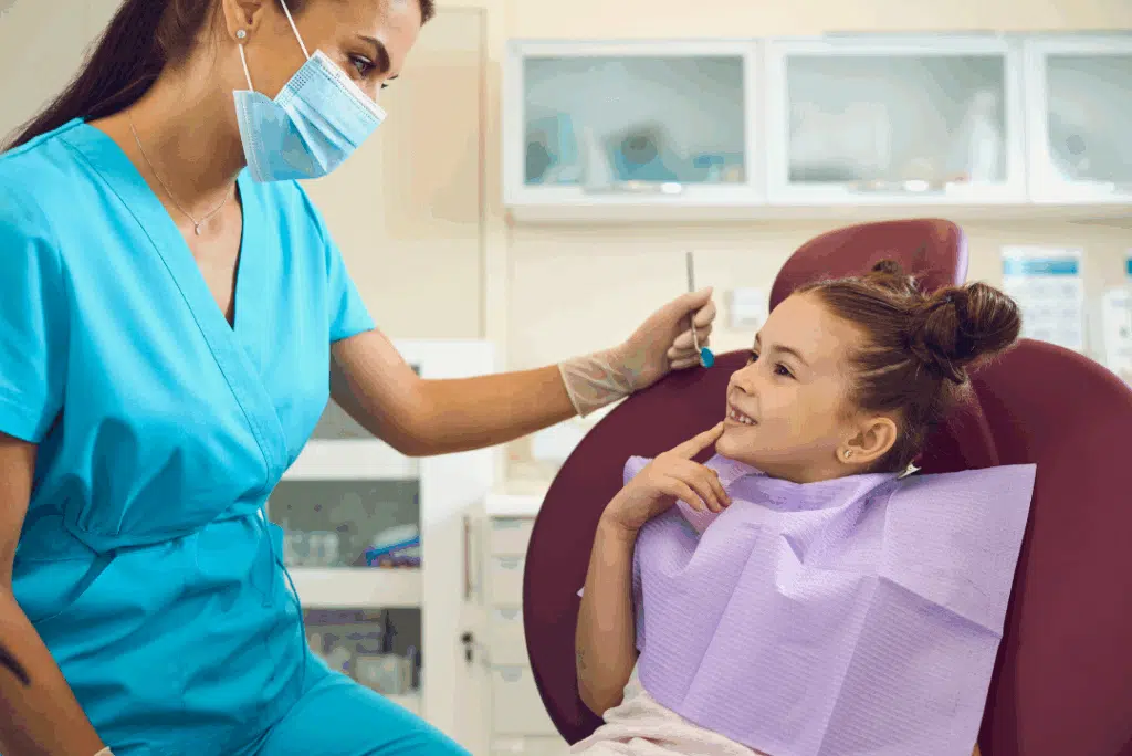 Pediatric Dentist In Great Neck, Ny: A Parent’s Guide To Expert Dental Care For Kids Pediatric dentist interacting with a smiling young girl during a dental checkup in a kid-friendly office setting.