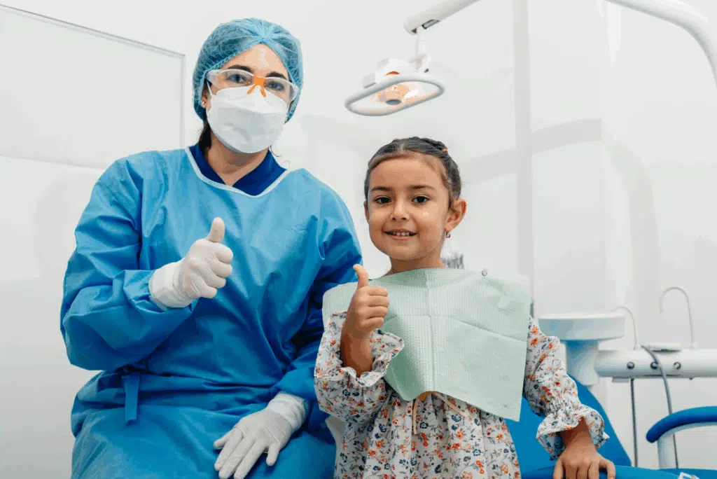 Pediatric Dentist In Great Neck, Ny: A Parent’s Guide To Expert Dental Care For Kids Child and pediatric dentist giving thumbs up in a dental office, promoting a positive dental experience at PCO Pediatric Dentistry & Orthodontics in Great Neck, NY.