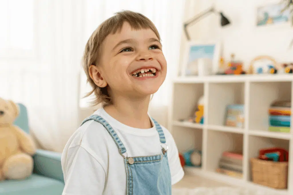 Dental Emergencies 101: What To Do When Your Child Chips, Cracks, Or Loses A Tooth (Before You Call The Dentist) Smiling child with missing front teeth in a bright, playful room, illustrating the importance of pediatric dental care for injuries.