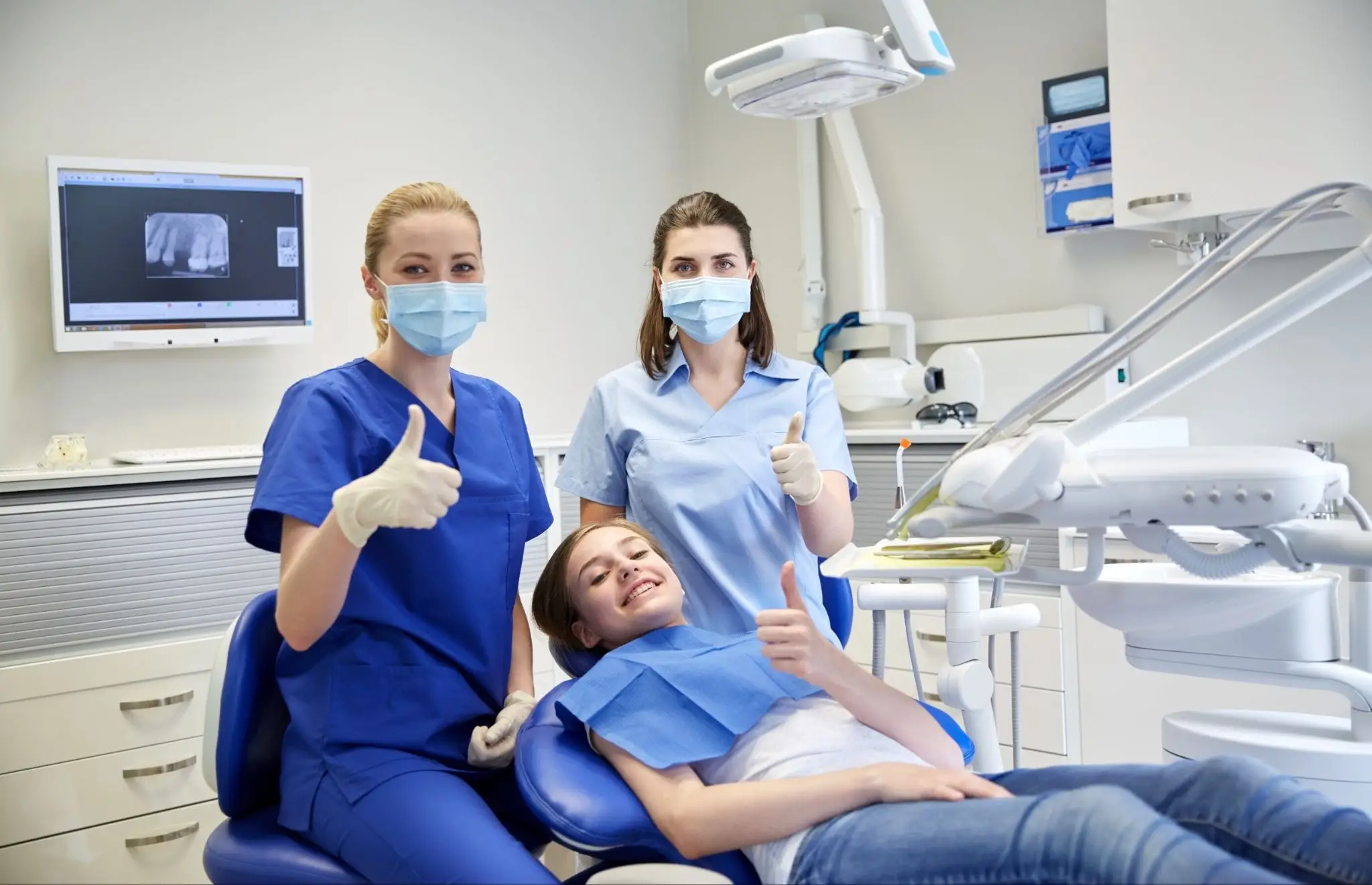 Female dentist with dental assistant treating a happy young girl patient at a modern dental clinic