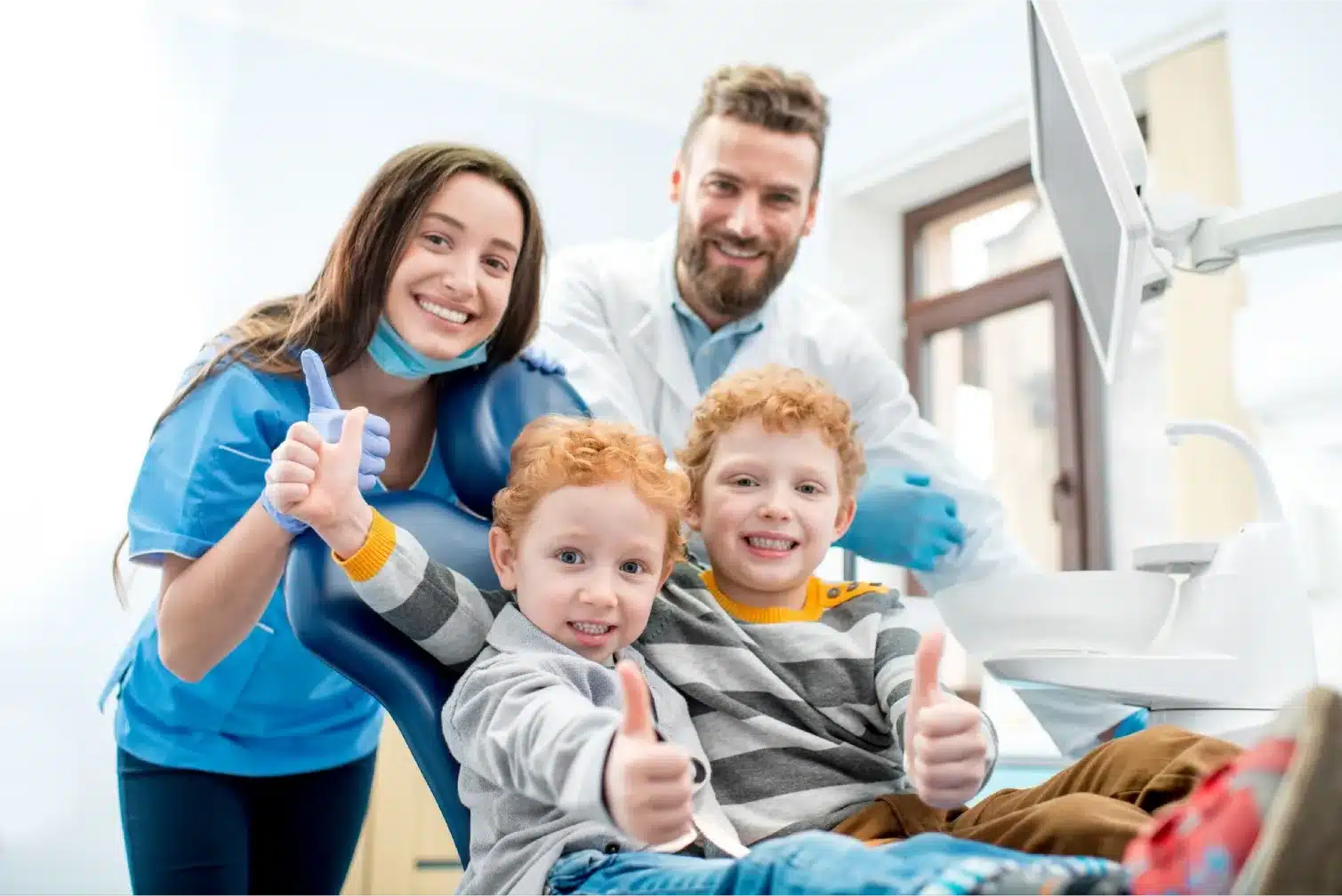 Happy young boys sitting in a dental chair with a dentist and assistant at the dental office